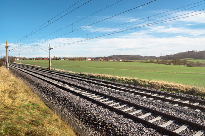 Two empty railway tracks under a blue sky, through nature. German railroad lines with a diminishing perspective. No traffic. By YesPhotographers via Shutterstock license.